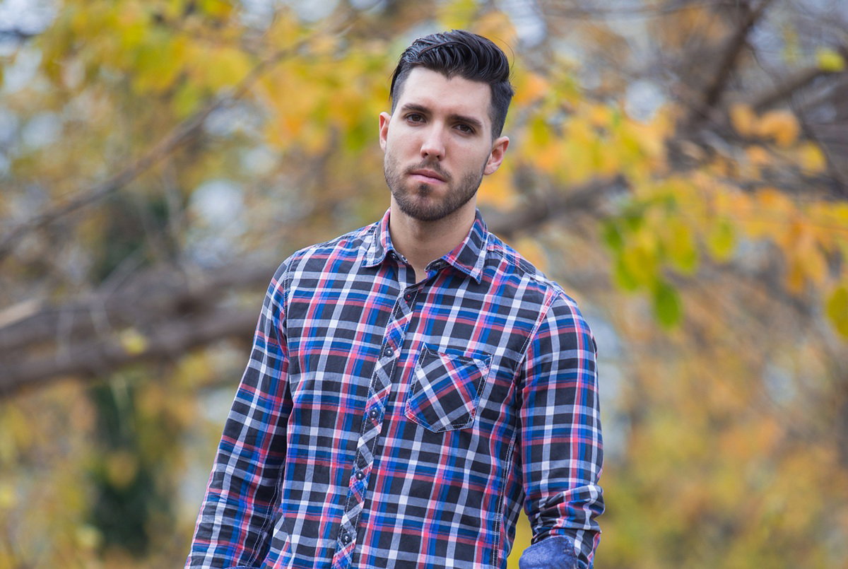 młody mężczyzna w wieku 25 plus w kraciastej koszuli stoi na tle jesiennego pejzażu smutny i zamyślony