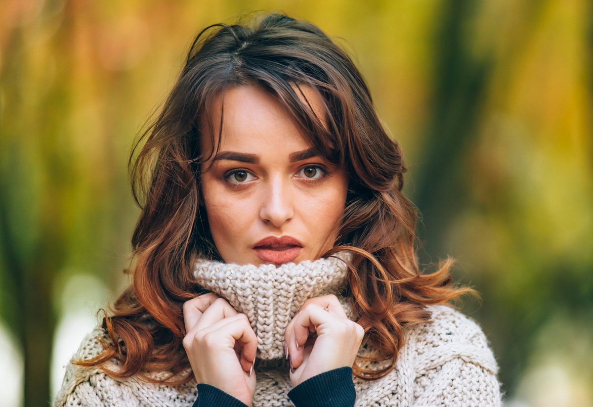 kobieta w wieku 30 plus w jasnym swetrze stoi zamyślona i smutna na zewnątrz