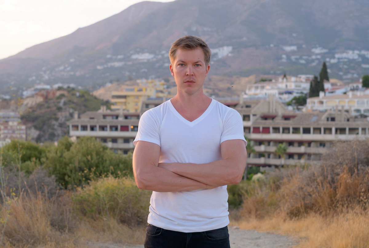 mężczyzna w wieku 30 plus w białym T-shircie stoi na tle krajobrazu Malagi w Hiszpanii