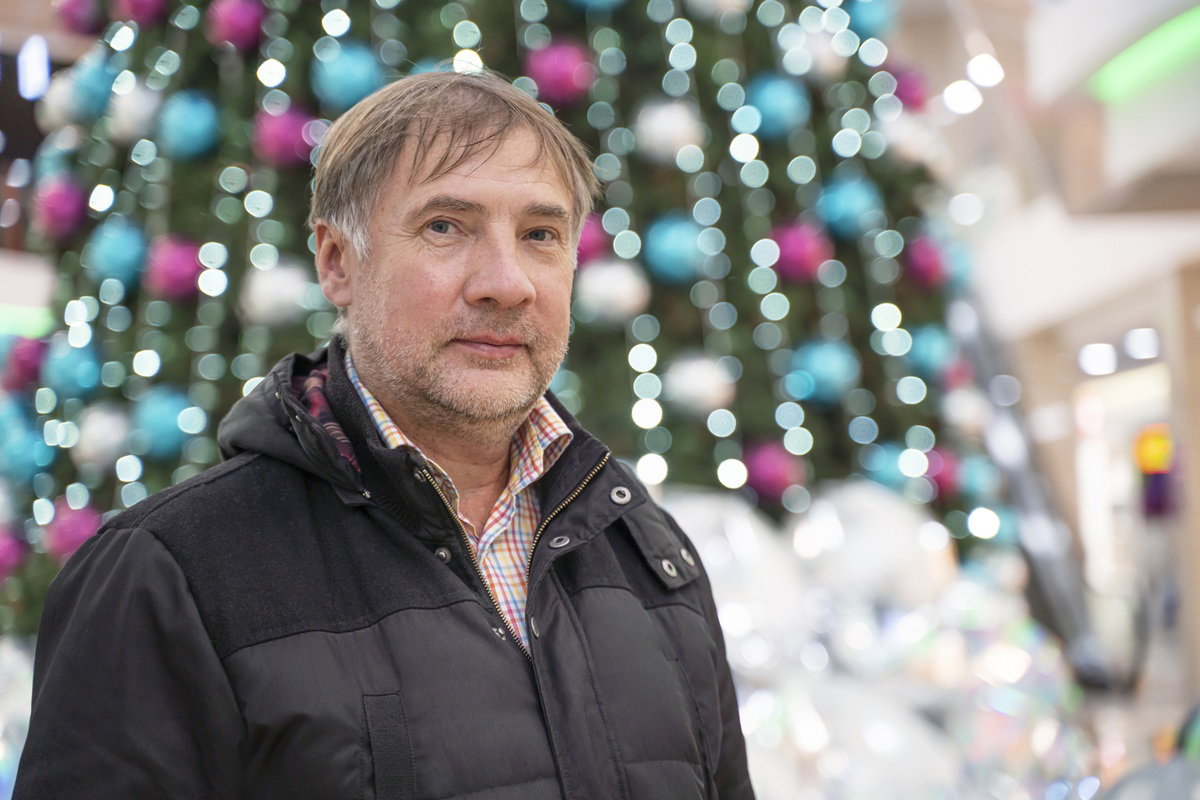 mężczyzna w wieku 50 plus z zarostem w czarnej kurtce stoi na tle choinki smutny i zamyślony