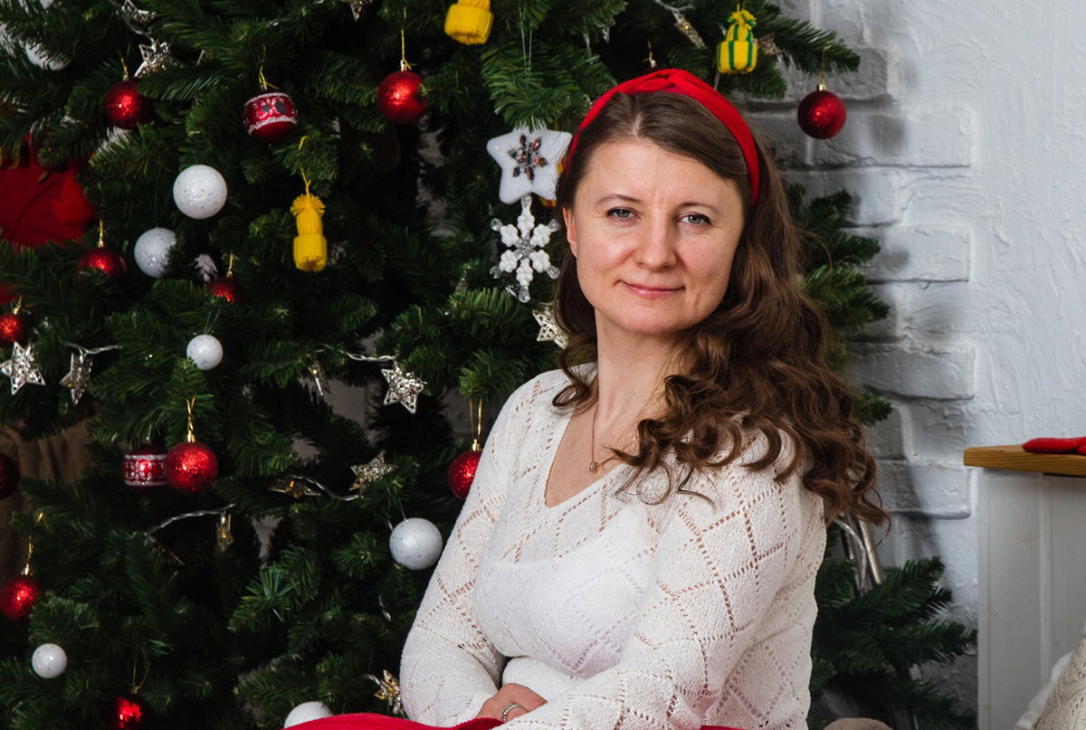 kobieta w wieku 35 plus siedzi na tle choinki i uśmiecha się powątpiewająco