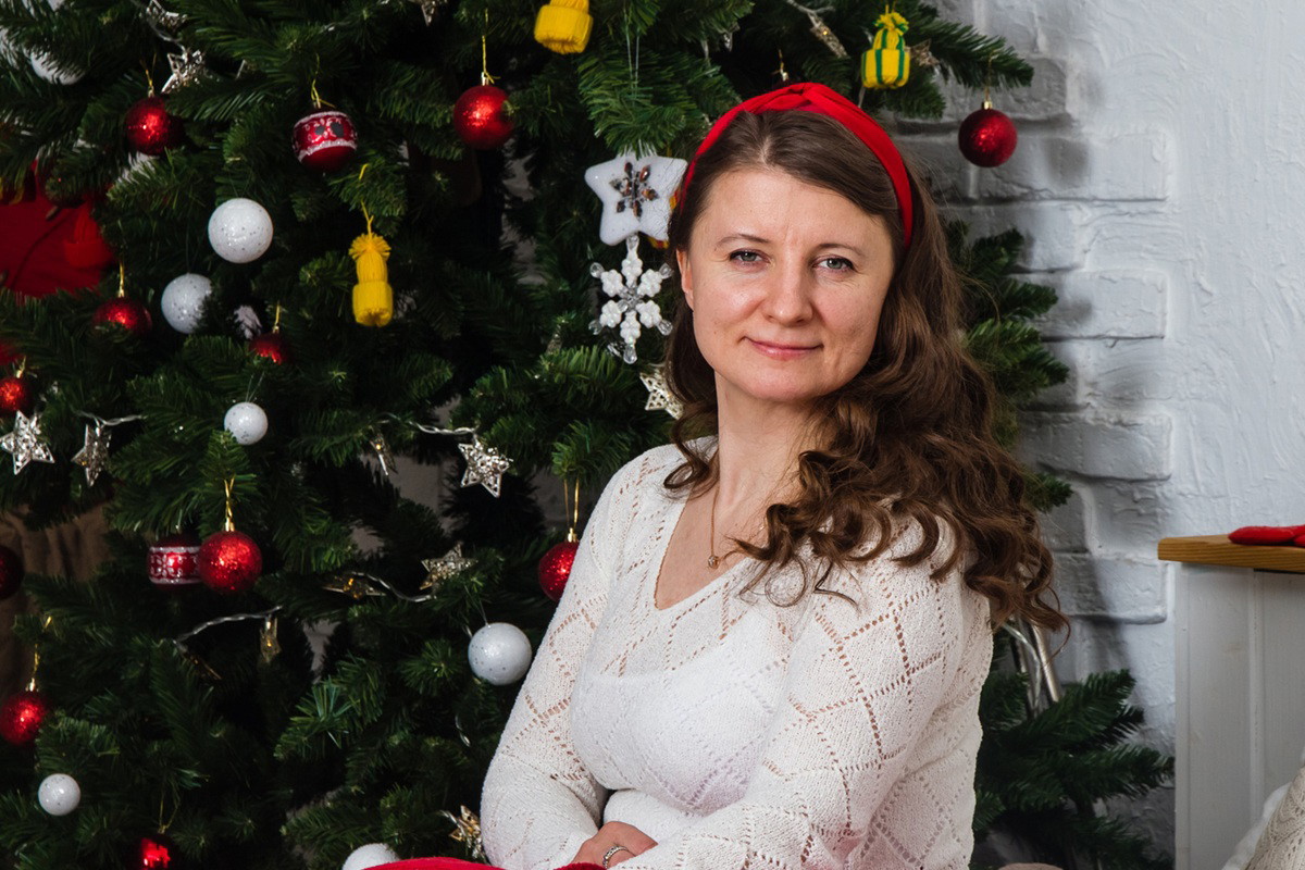 kobieta w wieku 35 plus siedzi na tle choinki i uśmiecha się powątpiewająco