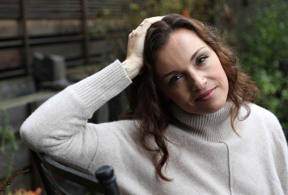 kobieta w wieku 40 lat w jasnym swetrze z golfem siedzi na tarasie zafrasowana i kpiąca