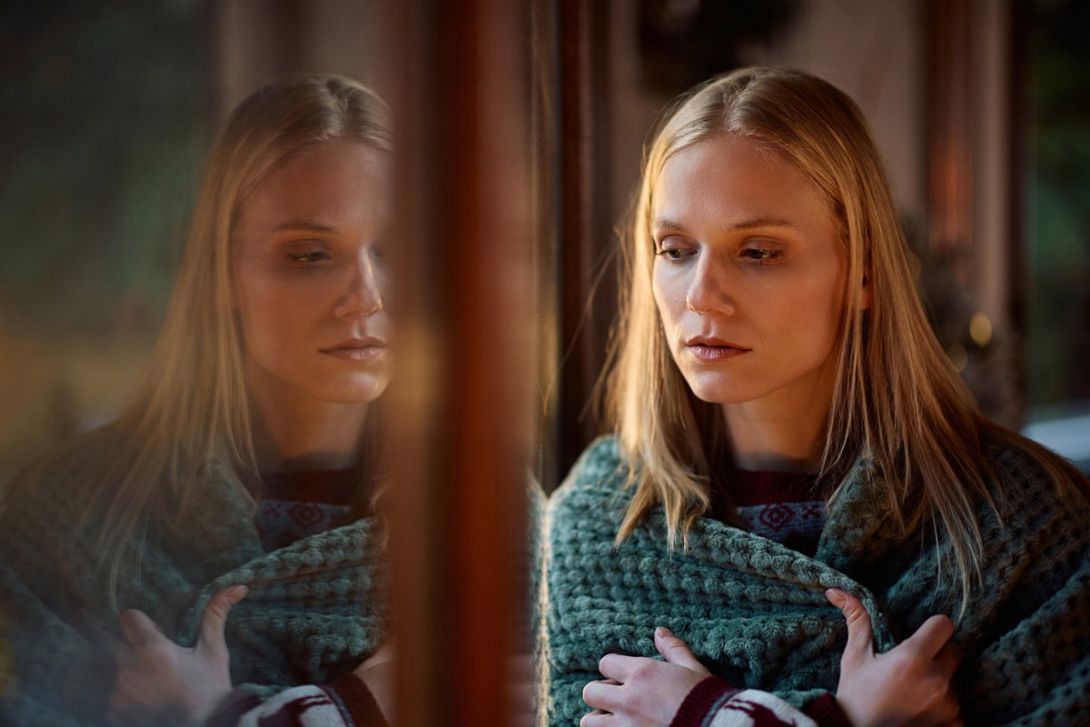 kobieta w wieku 25 plus blondynka stoi przy oknie w kocu smutna i zamyślona