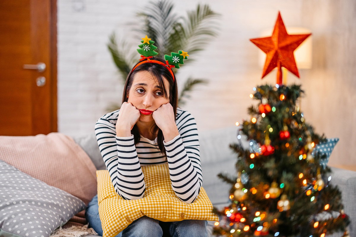 kobieta w wieku 35 plus siedzi na kanapie przy choince załamana
