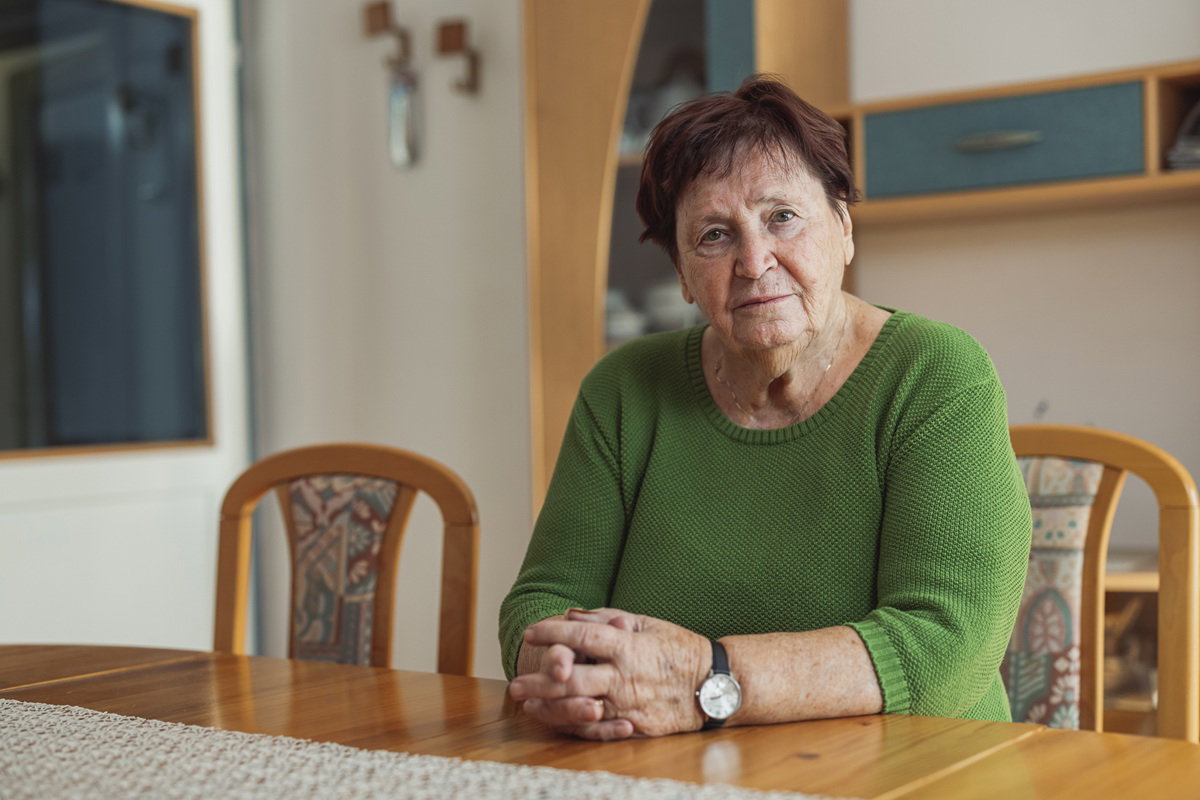 kobieta w wieku około 75 lat w zielonym sweterku siedzi przy stole zamyślona