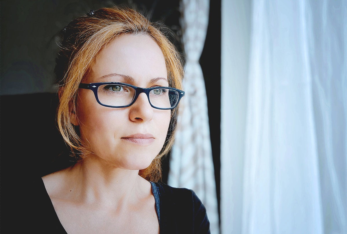 kobieta w wieku 40 plus w okularach stoi przy oknie zamyślona