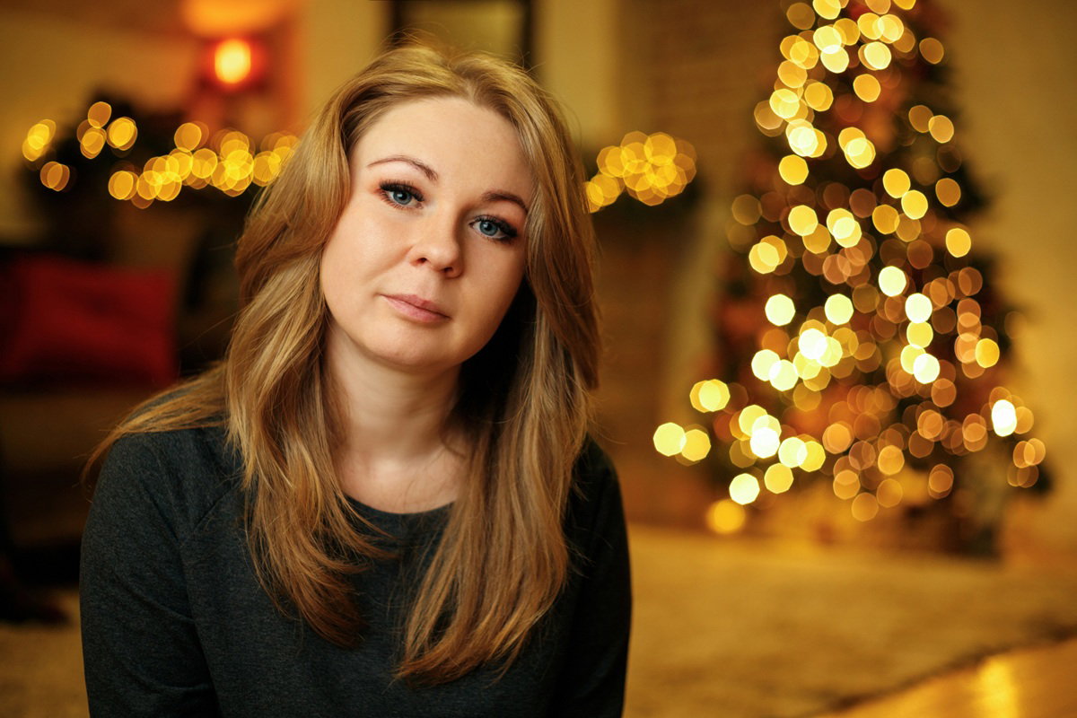 kobieta w wieku 30 plus blondynka siedzi na tle choinki smutna i zamyślona