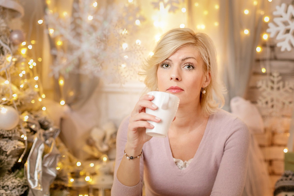kobieta w wieku 30 plus blondynka siedzi na tle świątecznych dekoracji z kubkiem herbaty