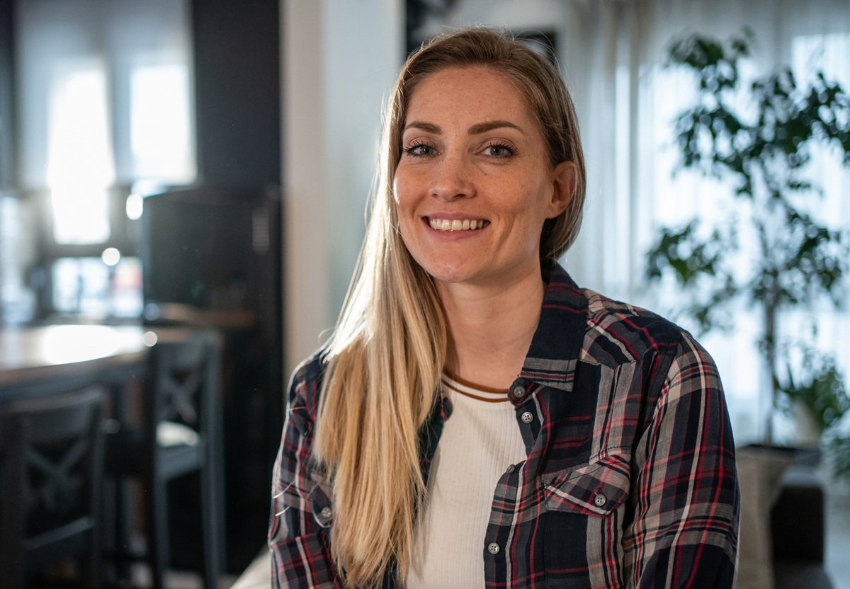 kobieta 30 plus blondynka w kraciastej koszuli stoi na tle kuchni i uśmiecha się z przekąsem