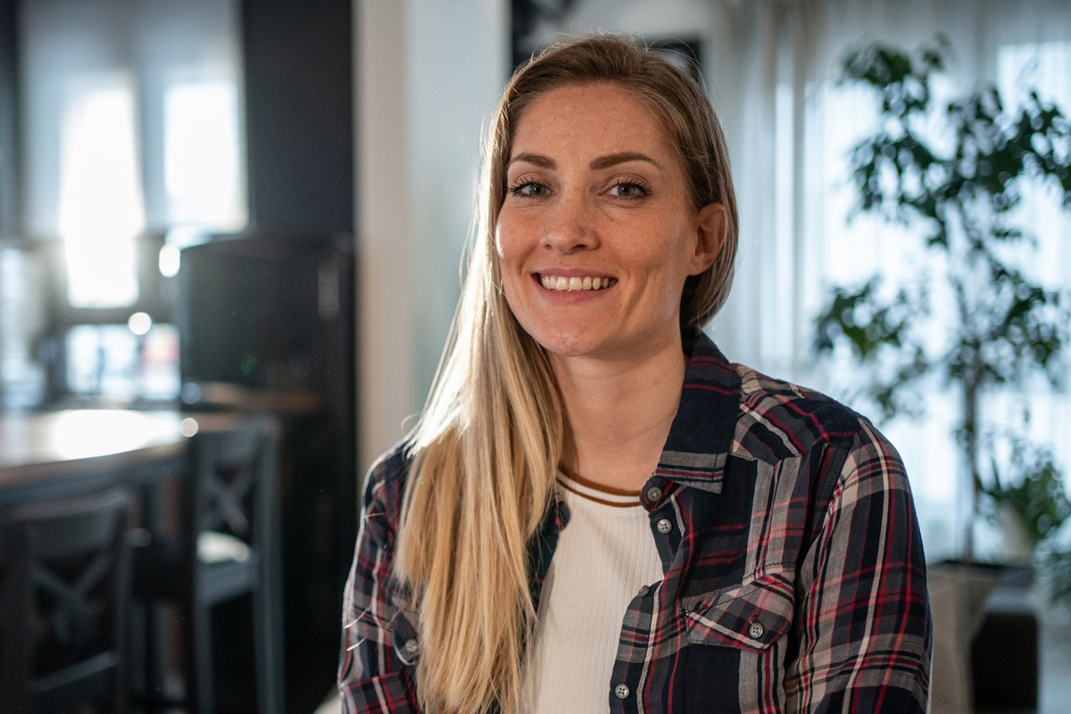 kobieta 30 plus blondynka w kraciastej koszuli stoi na tle kuchni i uśmiecha się z przekąsem