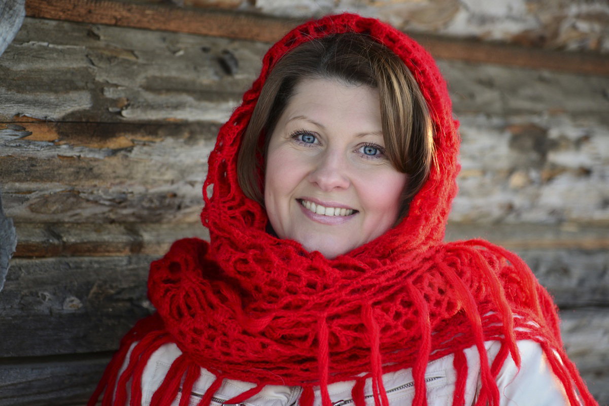 kobieta w wieku około 40 lat w czerwonej chuście na głowie stoi na tle drewnianej ściany i się uśmiecha