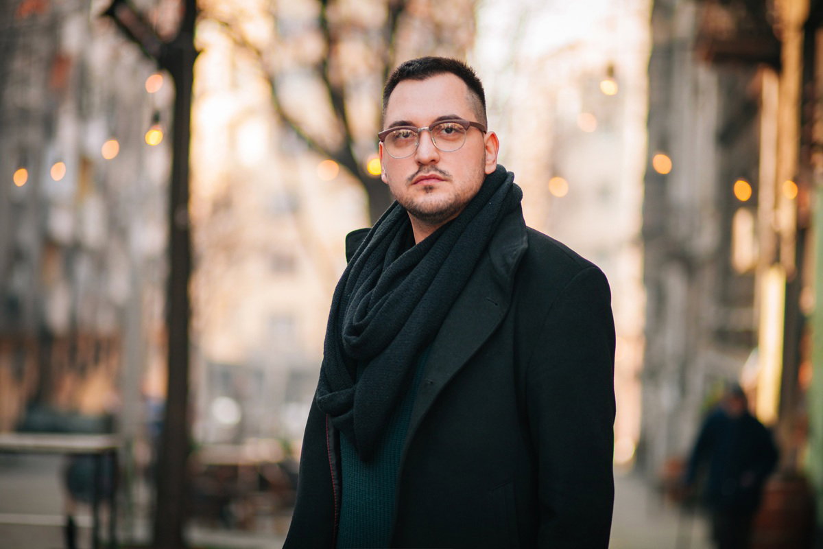 mężczyzna w wieku około 40 plus w okularach i czarnym płaszczu stoi na ulicy poważny