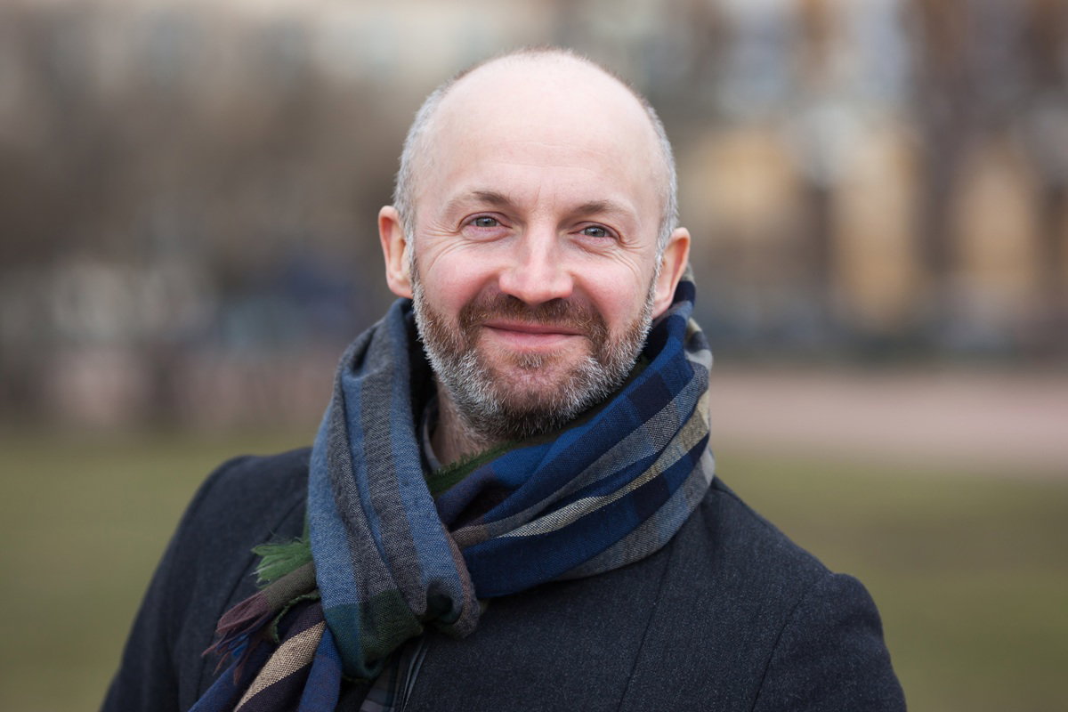 mężczyzna w wieku 45 plus z wąsami i brodą łysy stoi na zewnątrz i uśmiecha się szeroko