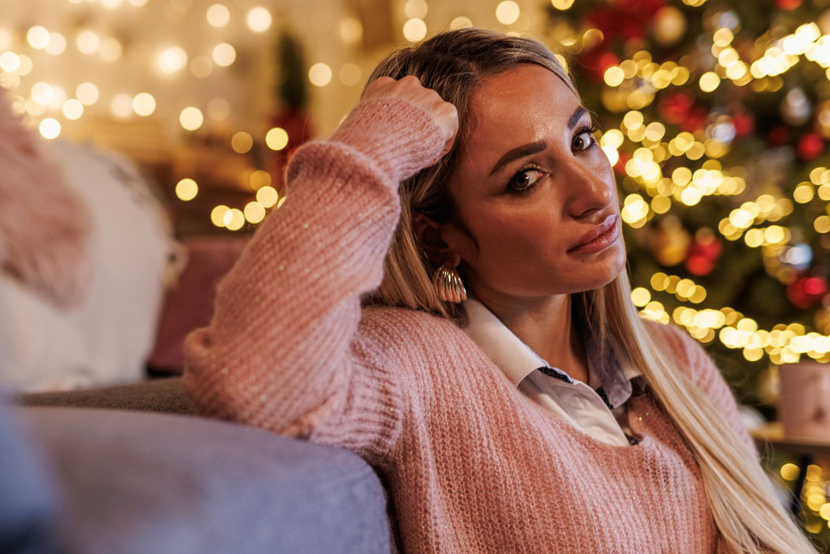 kobieta w wieku 30 plus w różowym swetrze siedzi na podłodze na tle choinki zdziwiona