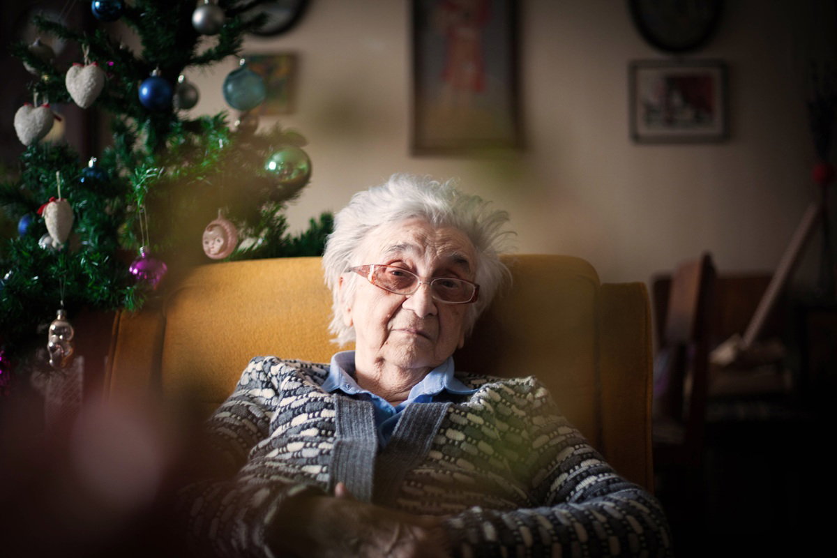 kobieta w wieku 80 plus w okularach siedzi w fotelu samotna przy choince