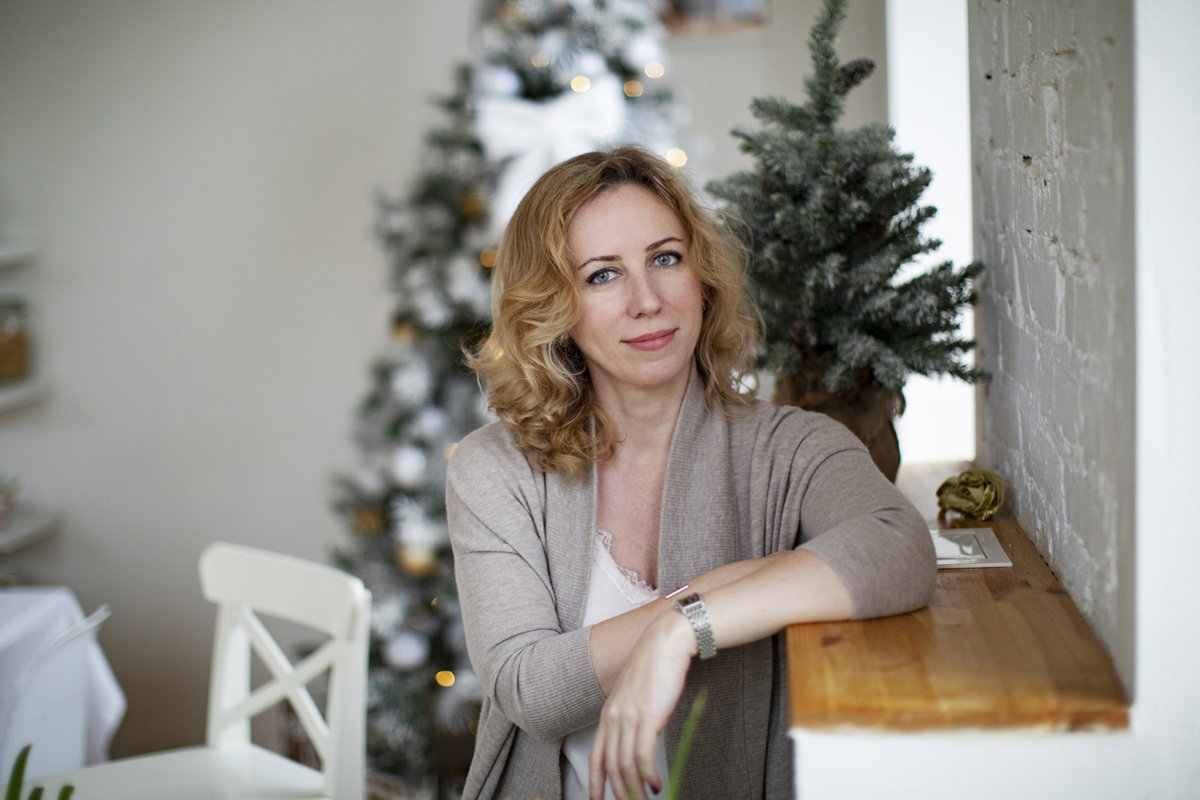 kobieta w wieku 35 plus stoi na tle choinki i uśmiecha się rozmarzona