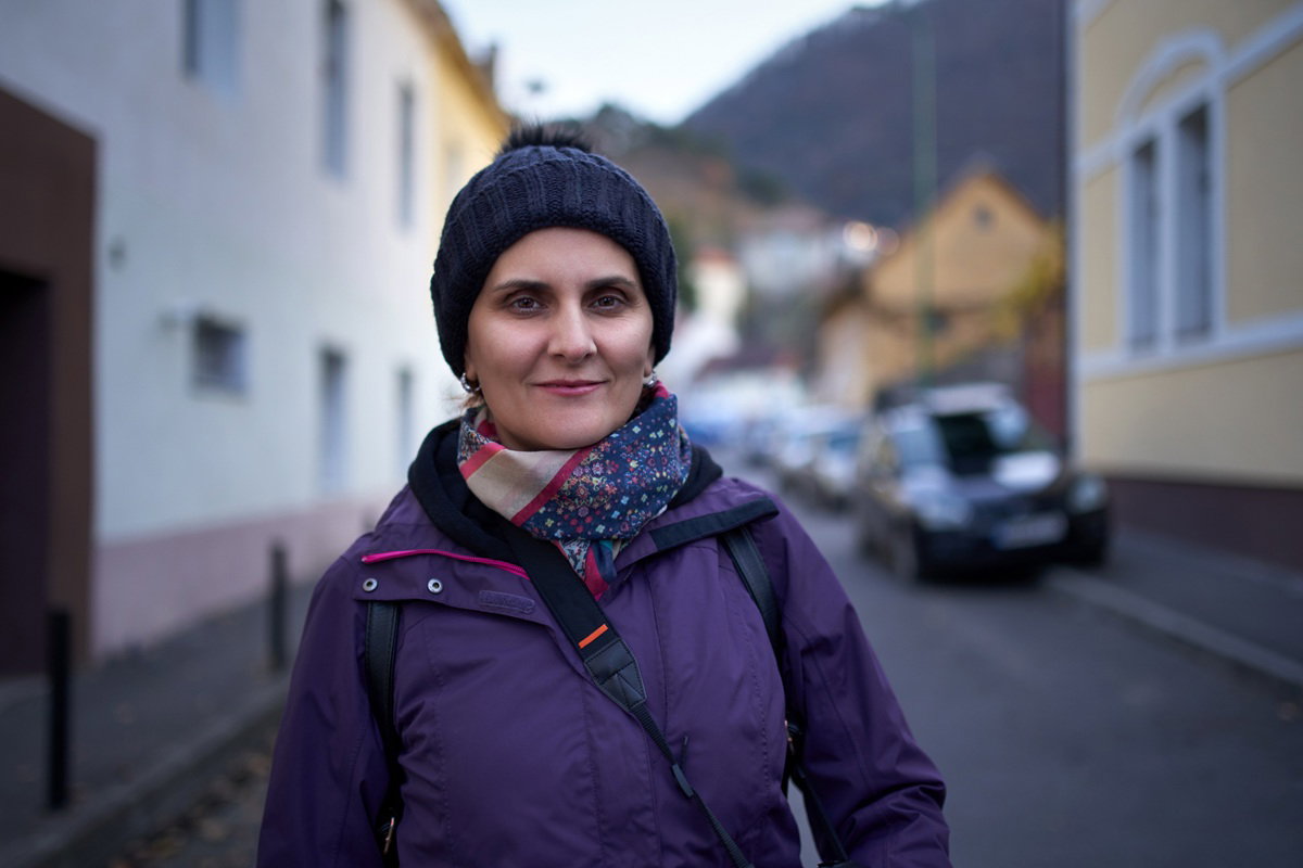 kobieta w wieku 30 plus w fioletowej kurtce i czapce stoi na ulicy w miasteczku na tle gór