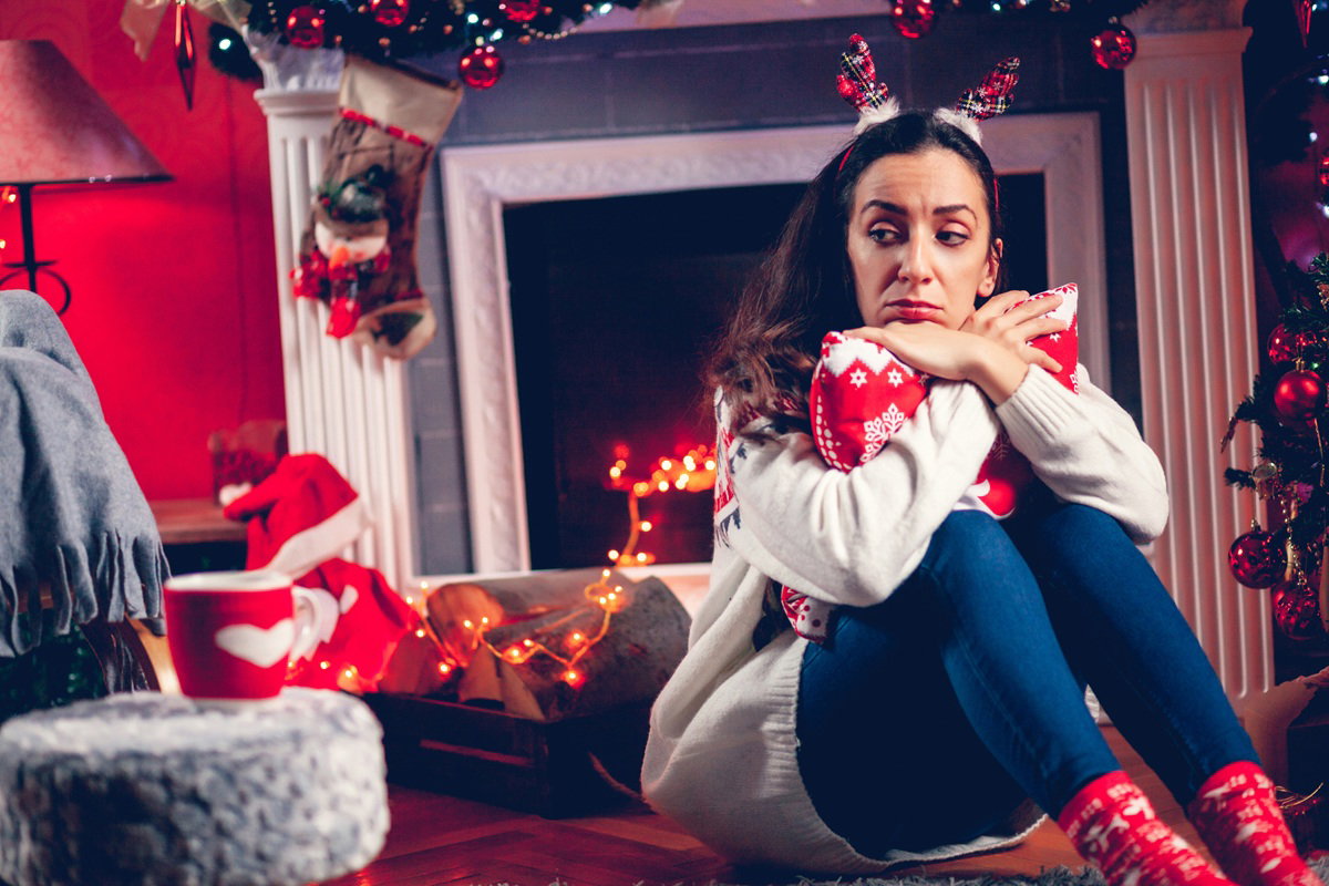 kobieta w wieku 35 plus siedzi na tle świątecznych dekoracji zrozpaczona i smutna