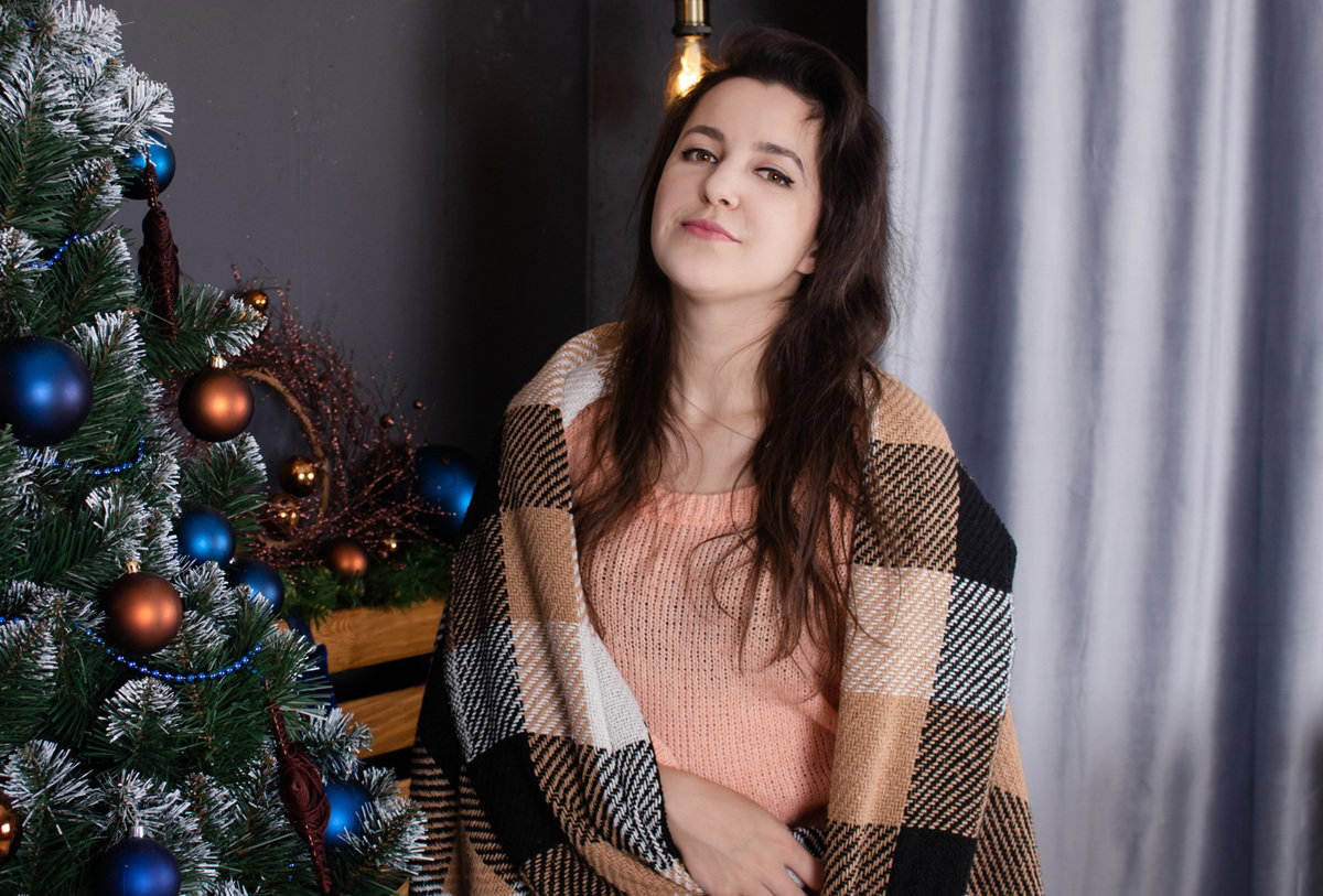 kobieta w wieku 30 plus stoi w kocu przy choince  poważnym wyrazem twarzy