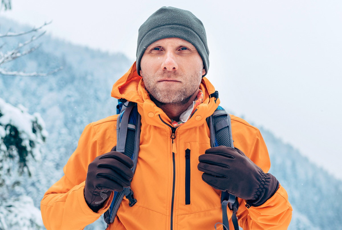 mężczyzna w wieku około 35 lat stoi na tle gór w pomarańczowej kurtce i patrzy poważnie
