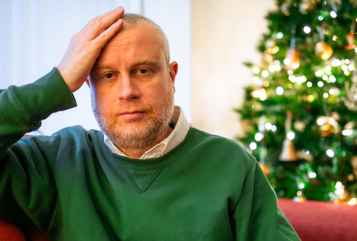 mężczyzna w zielonej bluzie siedzi na kanapie załamany na tle choinki