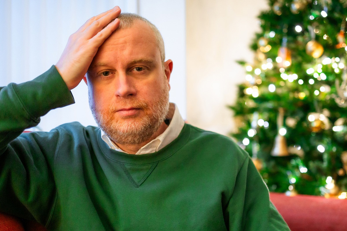 mężczyzna w zielonej bluzie siedzi na kanapie załamany na tle choinki