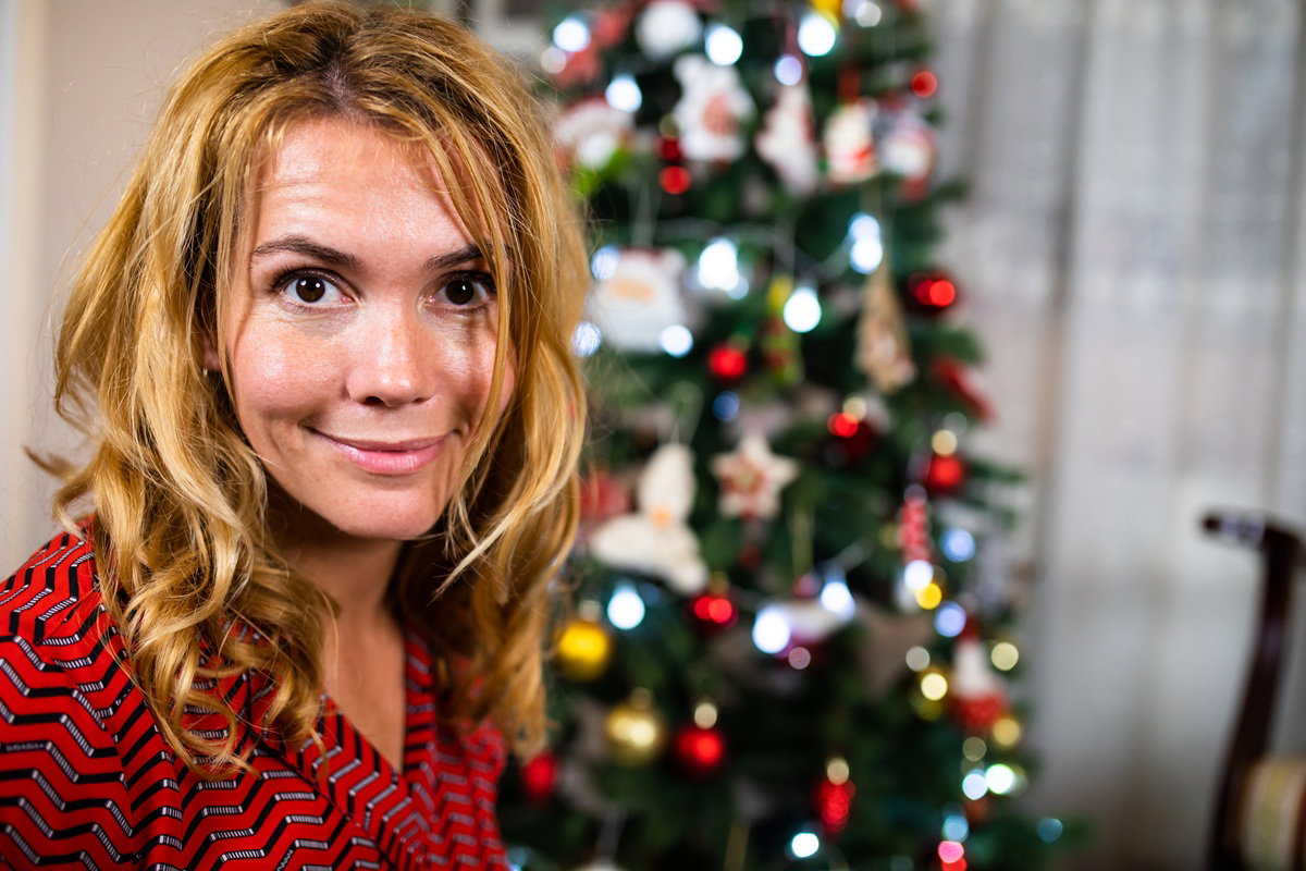 kobieta w wieku 30 plus stoi na tle choinki i uśmiecha się wymownie
