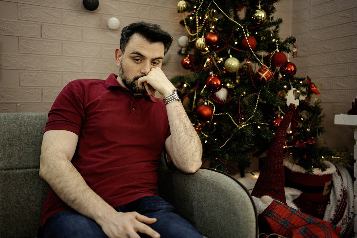 mężczyna w wieku około 30 lat siedzi przy choince na kanapie zafrasowany