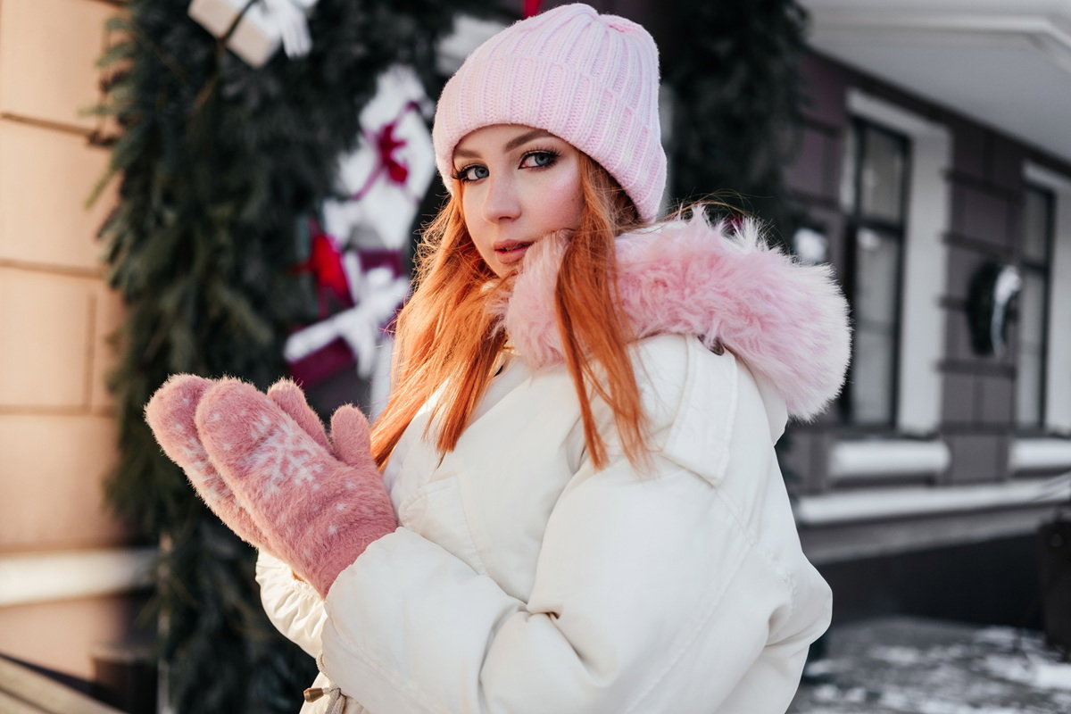 Ginger young woman in coat standing on street in front of fir branches gift boxes. Redhead girl 20 years old outdoors