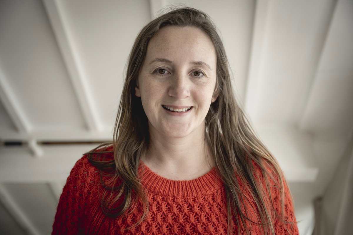 kobieta w wieku 35 plus w czerwonym swetrze stoi wewnątrz i lekko się uśmiecha