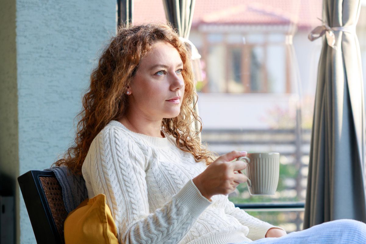 zamyslona kobieta w kubkiem w dłoni