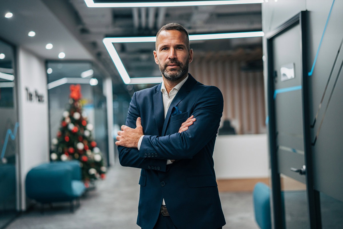 mężczyzna w wieku 40 plus z wąsami i brodą siwiejący w garniturze stoi w biurze na tle choinki smutny