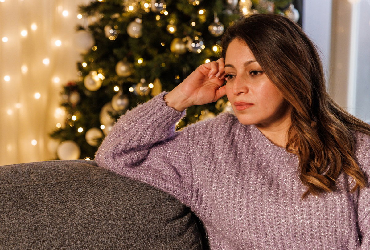 kobieta w wieku 30 plus siedzi na kanapie na tle choinki zdegustowana