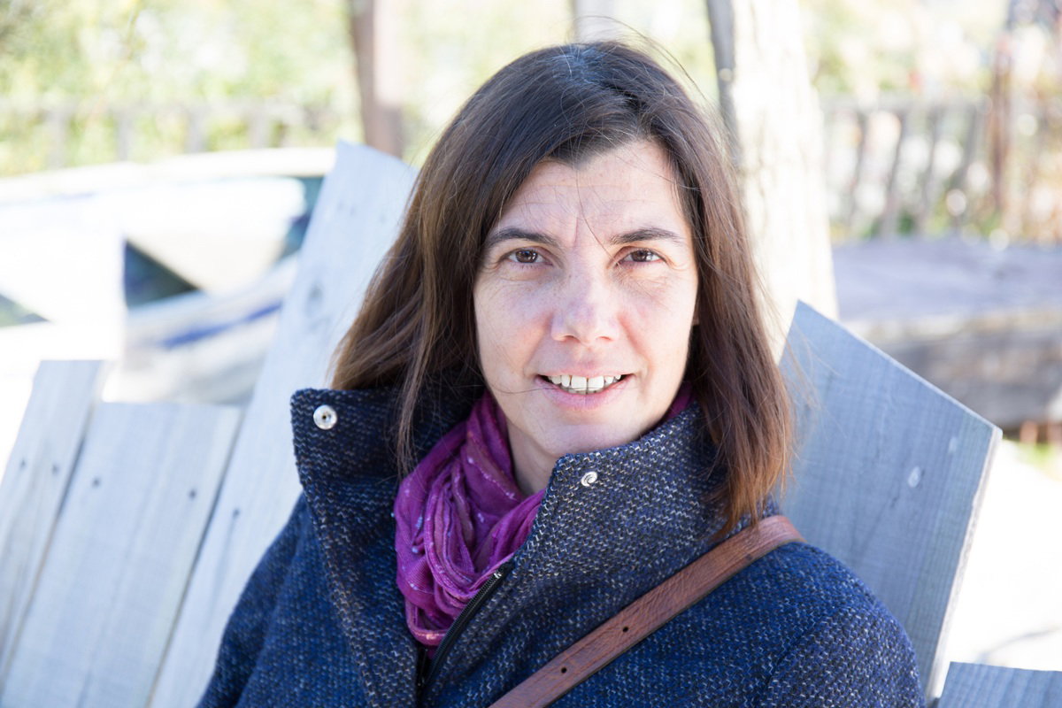 kobieta w wieku około 40 lat siedzi na zewnątrz w płaszczu i patrzy poważnym spojrzeniem