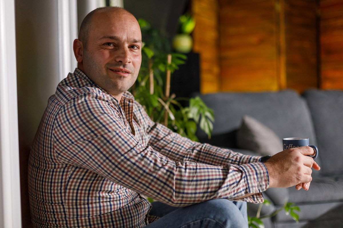 mężczyzna w wieku 40 plus w koszuli w kratkę siediz w salonie z kpiącym uśmiechem