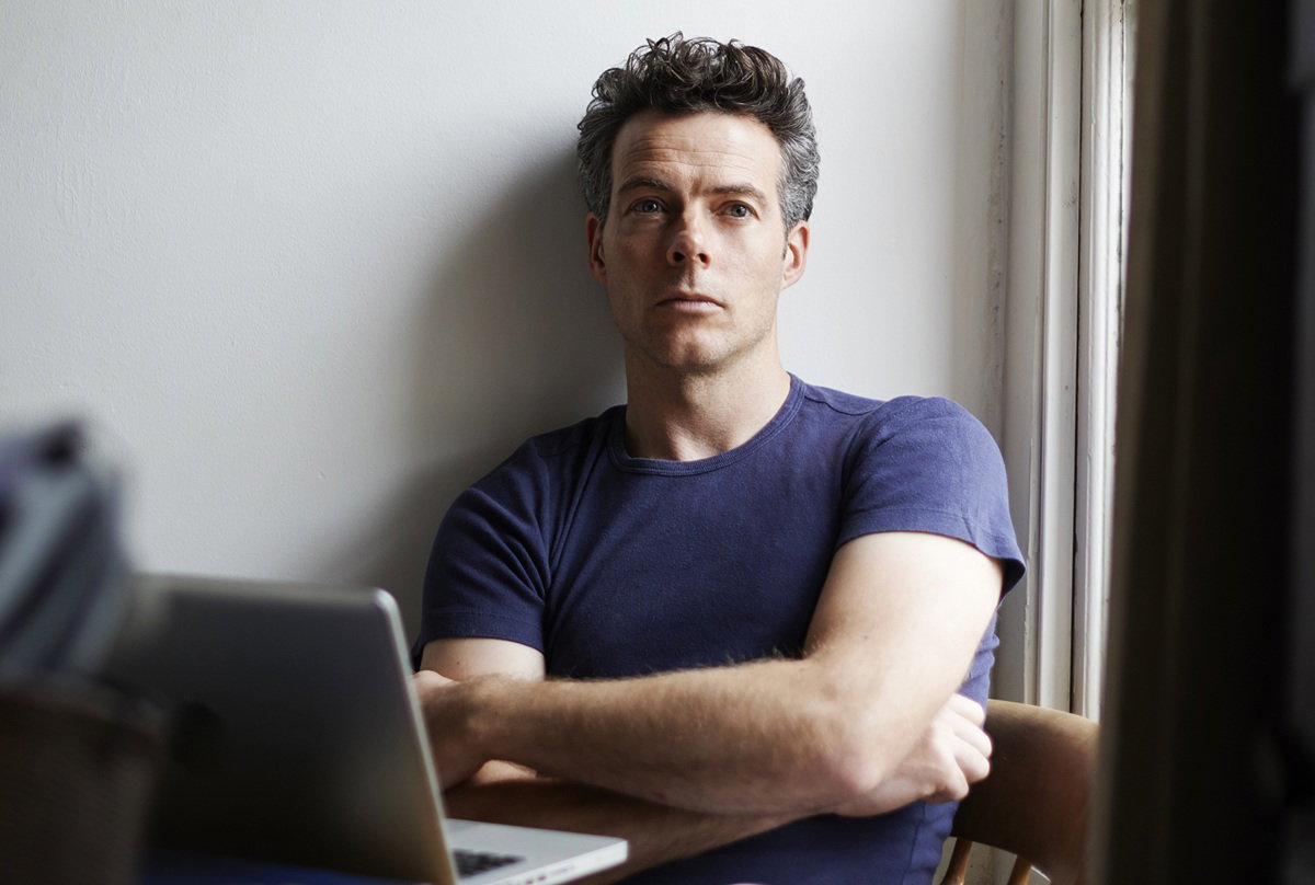 mężczyzna w wieku 45 plus siedzi z laptopem zamyślony i smutny