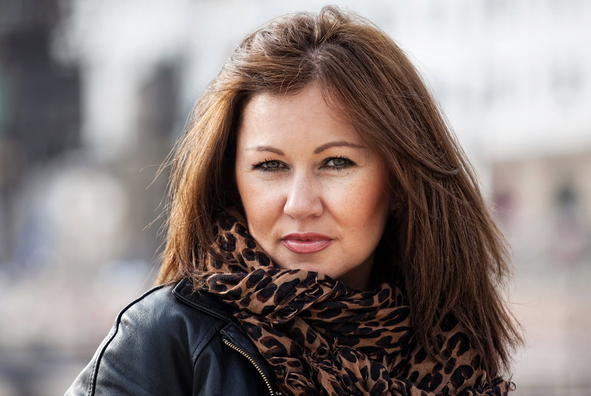 kobieta w wieku 35 plus w szalu w panterkę i skórzanej kurtce patrzy rozmarzonym wzrokiem