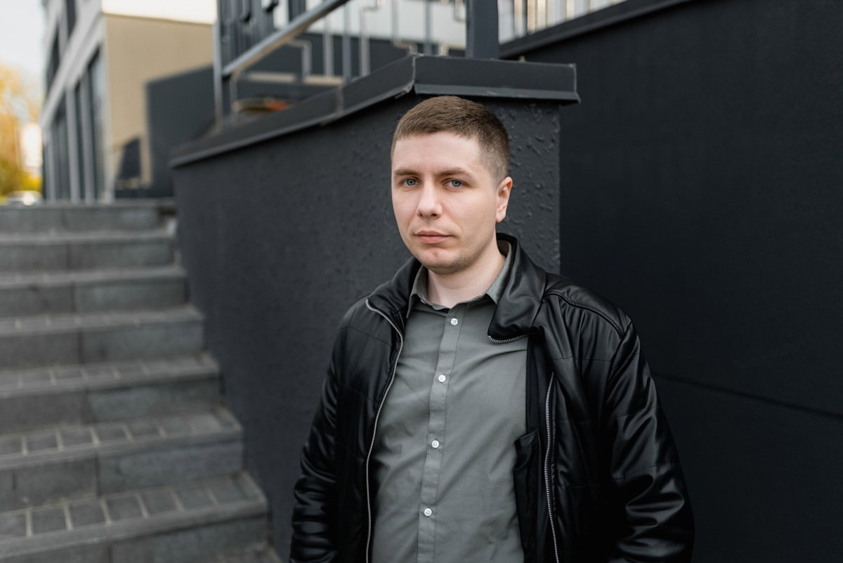 mężczyzna w wieku 25 plus blondyn w skórzanej kurtce stoi na tle budynku smutny