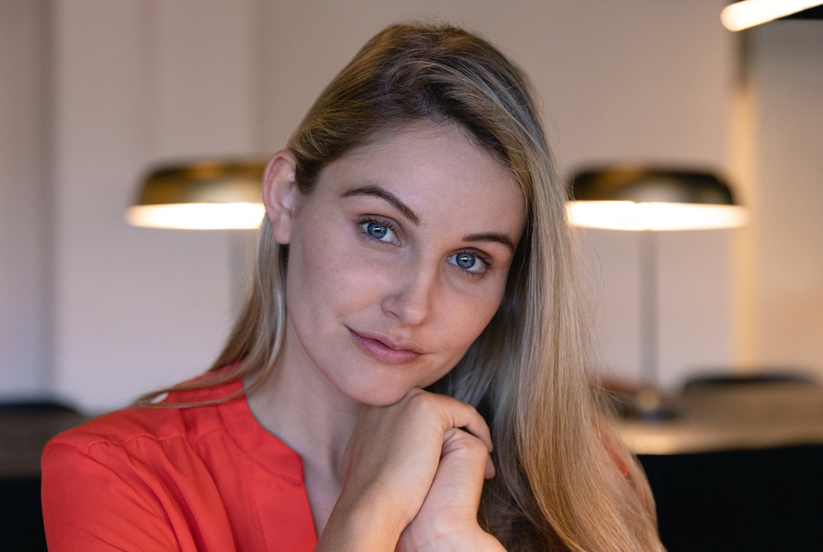 kobieta w wieku 25 plus blondynka w czerwonej bluzce stoi wewnątrz nieco zmieszana