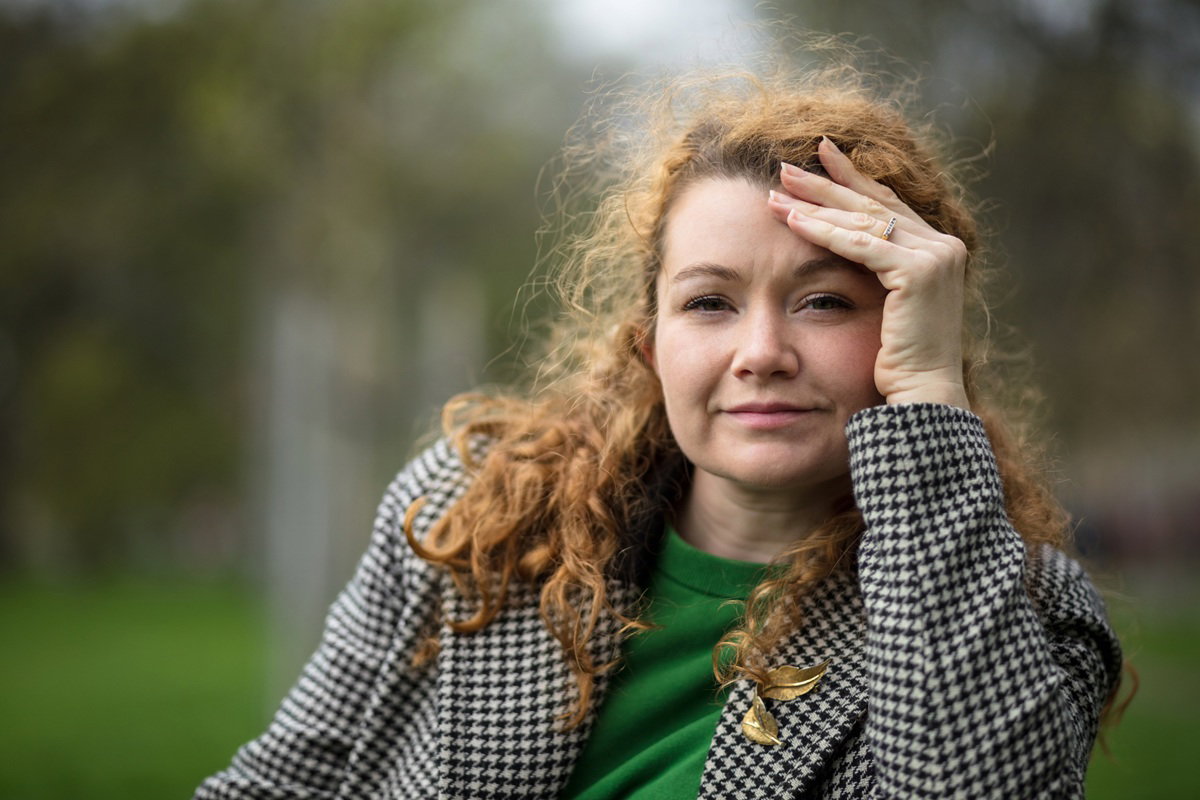 kobieta w wieku 30 plus z kręconymi rudymi włosami siedzi na ławce zamyślona i trzyma się za głowę