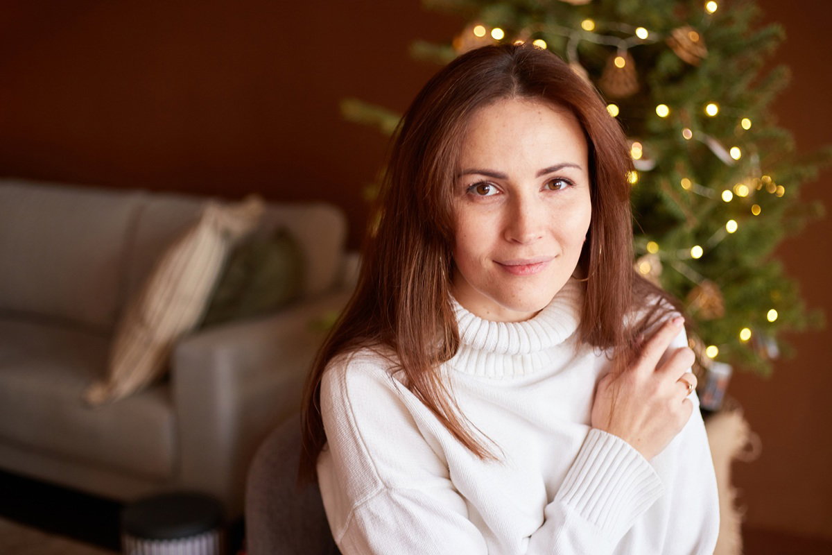 kobieta w wieku 35 plus w jasnym swetrze na tle choinki lekko się uśmiecha zamyślona