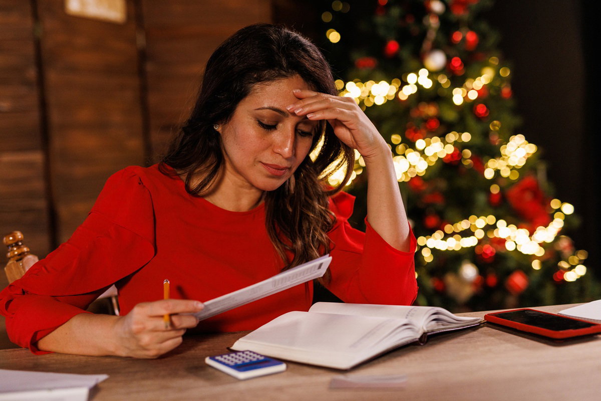 kobieta w wieku 35 plus siedzi przy choince nad rachunkami zafrasowana