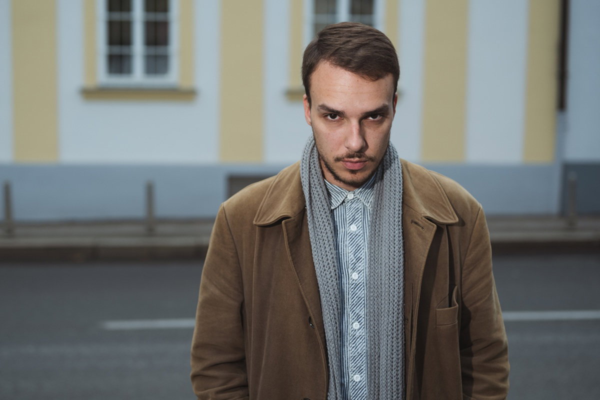 mężczyzna w wieku 25 plus w płaszcz stoi na tle budynku zafrasowany i zamyślony
