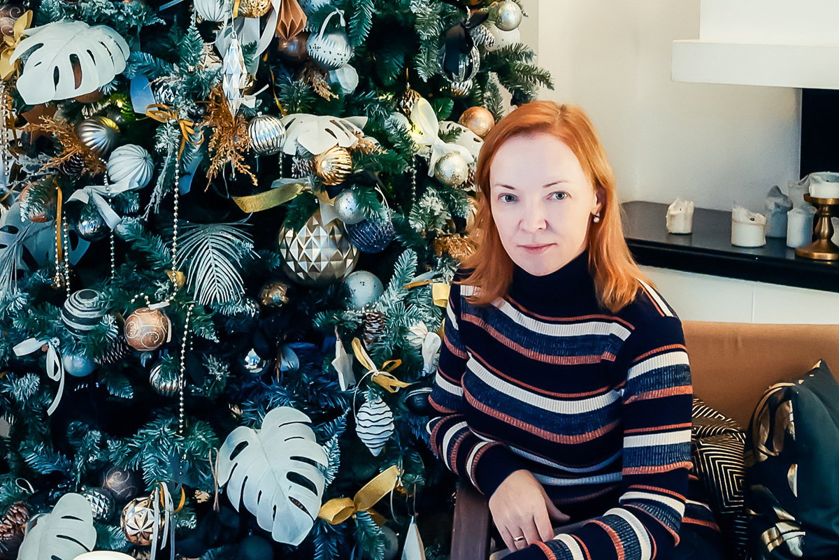 kobieta w wieku 40 plus siedzi przy bogato przystrojonej choince zamyślona i smutna