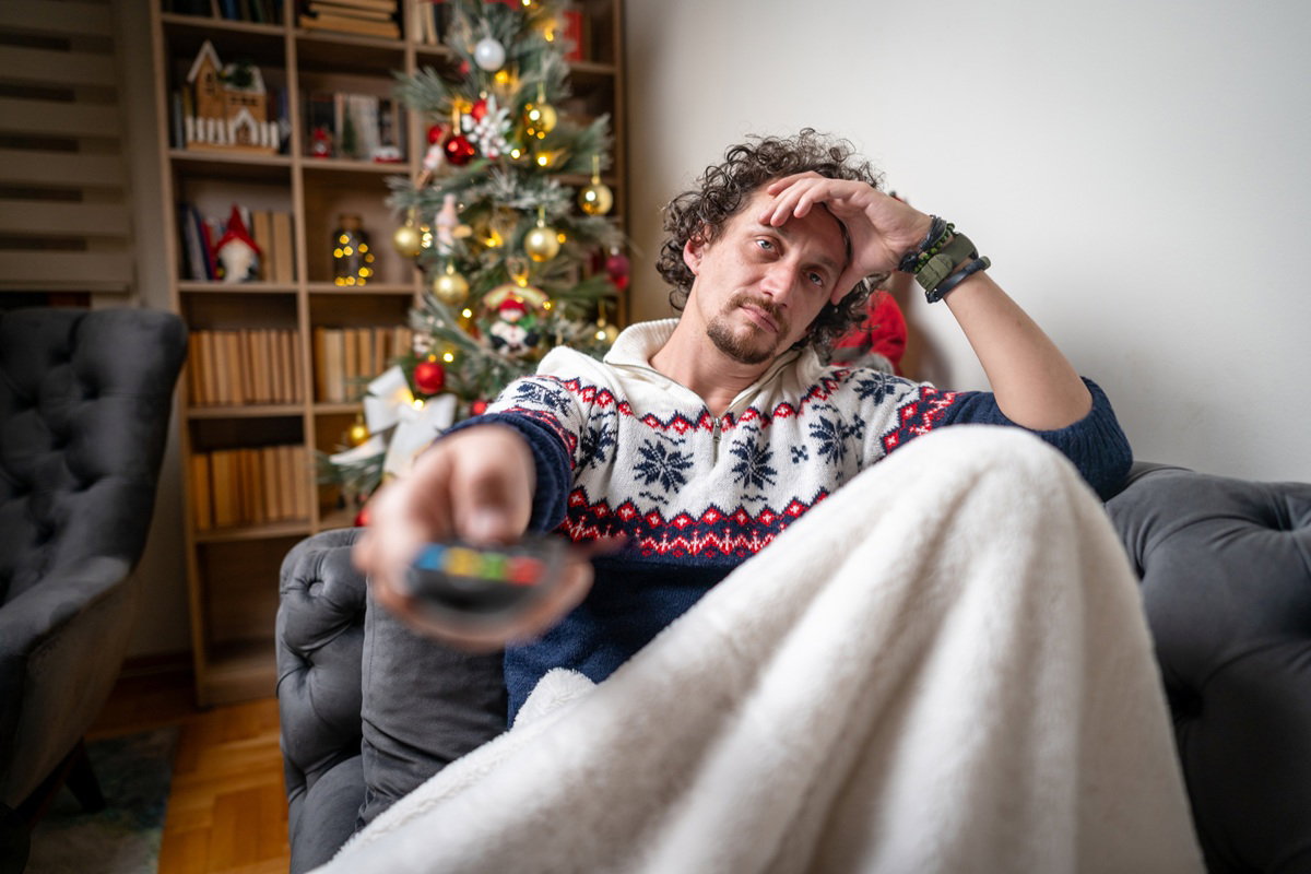 mężczyzna w wieku 30 plus siedzi na kanapie z pilotem w ręku ze znudzoną miną