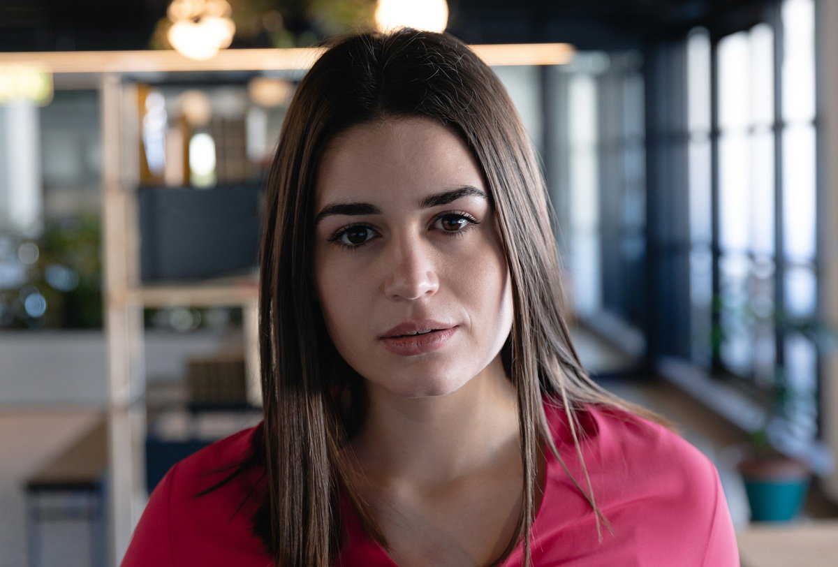 kobieta w wieku 30 plus w czerwonej bluzce z długimi włosami stoi na tle biura smutna