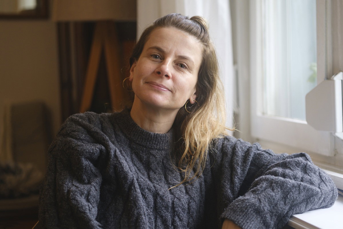 kobieta w wieku 40 plus w szarym swetrze siedzi przy oknie z zawiedzionym wyrazem twarzy