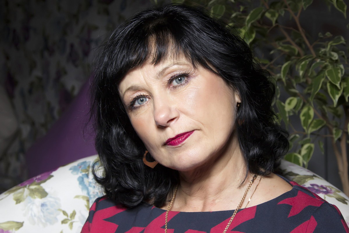 kobieta w wieku 50 plus czarne włosy siedzi na fotelu ze smutnym wyrazem twarzy