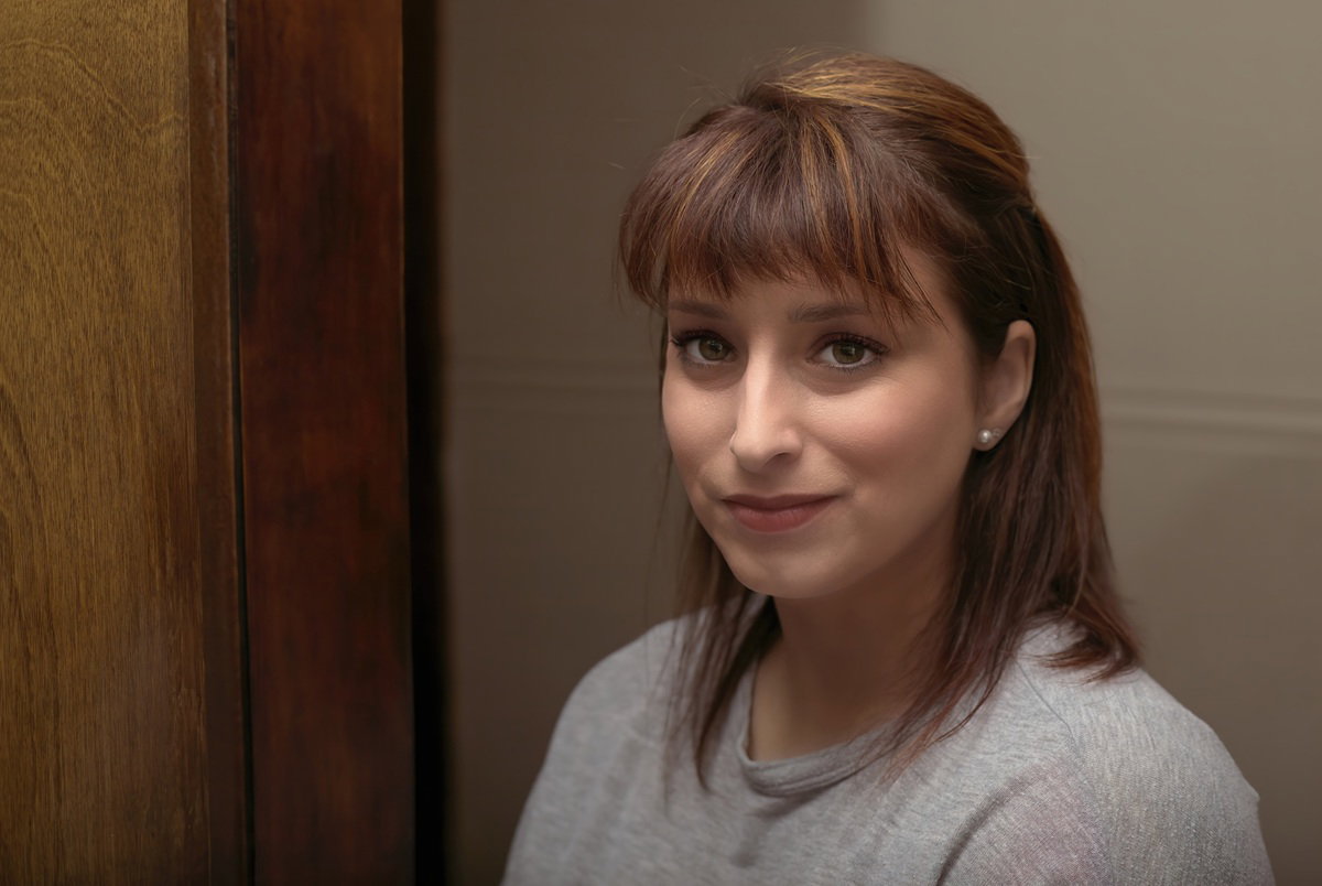 kobieta w wieku 35 plus stoi z niewyraźnym wyrazem twarzy koło drewnianej framugi